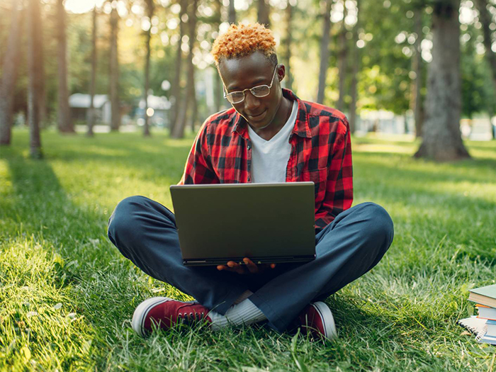 young person sitting in grass with computer
